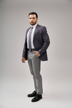 Gri arka planda el ele poz veren şık ve şık takım elbiseli yakışıklı bir adam.