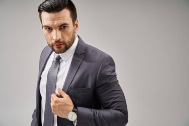 Gri arka plandaki kameraya bakarak kendine güvenen takım elbiseli karizmatik bir işadamı.
