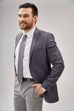 Gri arka planda elleri ceplerinde şık giyinmiş neşeli iş adamının portresi.