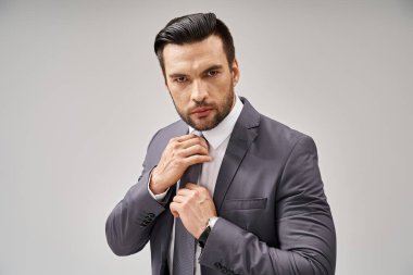 Resmi giyinmiş düşünceli bir adam kravatını gri arka planda, şirket modasında düzeltiyor.