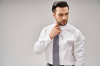 Beyaz gömlekli yakışıklı işadamının portresi gri arka planda kravatını düzeltiyor, şık giyiniyor.