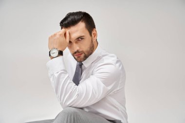 İyi giyimli ve resmi giyinmiş yakışıklı iş adamı gri geçmişiyle stüdyoda yerde oturuyor.