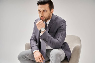 Gri arka planda rahat koltukta oturan şık takım elbiseli yakışıklı iş adamı.