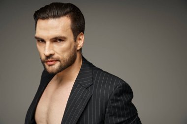 30 'lu yaşlardaki esmer adamın portresi. Gri arka planda ince çizgili takım elbiseli çıplak göğüs pozu.
