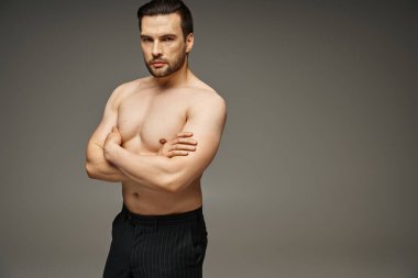 Esmer ve çıplak göğüslü yakışıklı bir adamın portresi. Gri arka planda çapraz kollarla poz veriyor.