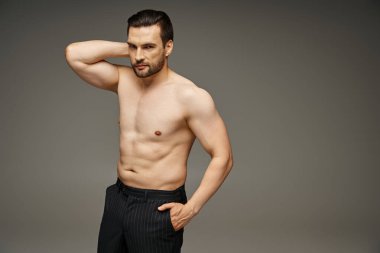 Gri arka planda el ele poz veren çıplak göğüslü esmer yakışıklı bir adamın portresi.