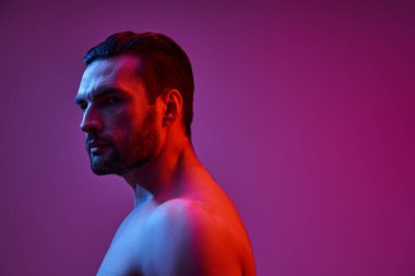 Mor arka planda kırmızı ve mavi ışıklarla poz veren seksi ve kaslı adamın portresi