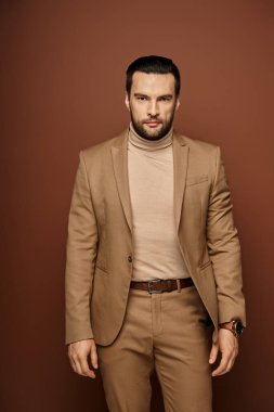 Kendine güveni olan, şık takım elbiseli, bej arka planda poz veren yakışıklı bir adamın portresi.
