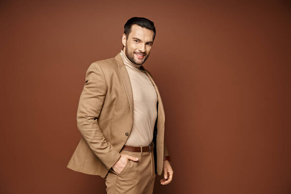 cheerful man with bristle posing in stylish beige blazer with hand in pocket on beige backdrop