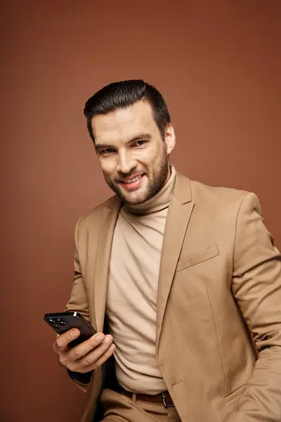 stock image Stylish and handsome man with bristle smiling and holding smartphone on beige backdrop, social media