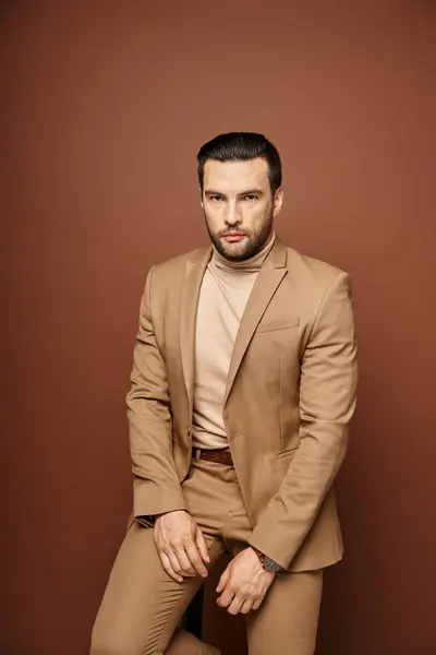 stock image handsome man in elegant attire looking at camera while sitting on chair on beige background