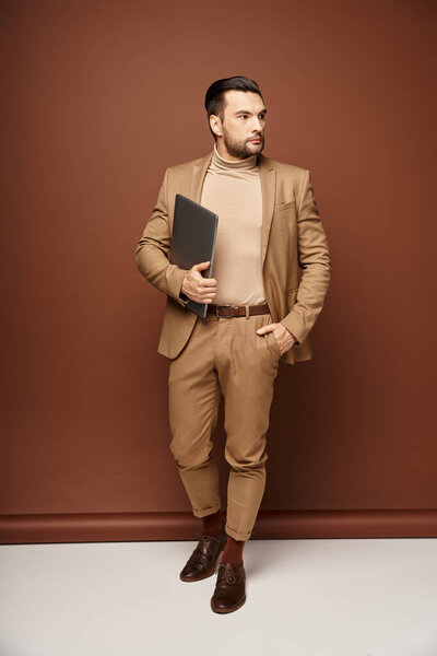 handsome businessman in elegant attire walking with his laptop on beige background, remote work
