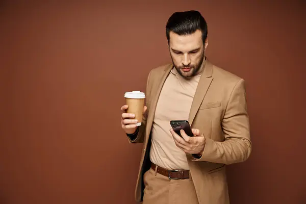Mann Stilig Antrekk Holder Kaffe Bruke Sin Smarttelefon Beige Bakgrunn – stockfoto