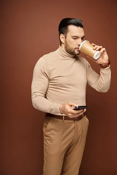 タートルネックのハンサムな男はコーヒーを飲んで ベージュの背景でスマートフォンを使用して ソーシャルメディア — ストック写真