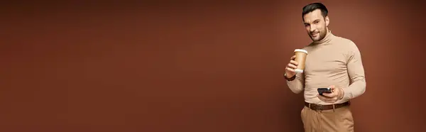 Счастливый Человек Водолазке Пьет Кофе Использует Свой Смартфон Бежевом Фоне — стоковое фото