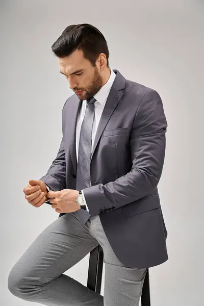 stock image handsome and confident businessman in suit sitting on high stool on grey background, leadership