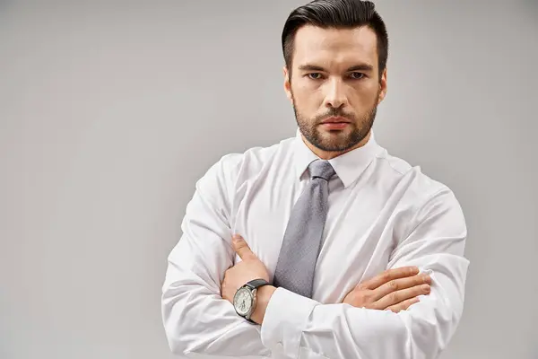 stock image portrait of serious businessman in suit standing with crossed arms while posing on grey background