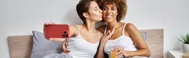 Mutlu kadın selfie çekiyor ve bir bardak portakal suyu ve pankartıyla Afrikalı Amerikalı kız arkadaşını öpüyor.