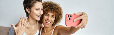 Mutlu ve nişanlı lezbiyen çift evde akıllı telefondan selfie çekiyor, afiş.