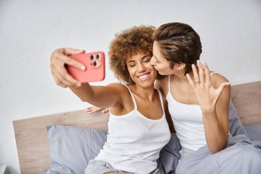 Mutlu ve nişanlı lezbiyen çift evde akıllı telefondan selfie çekiyor. Nişan yüzüğü.