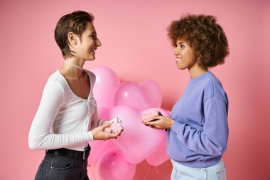 Sevgililer Günü 'nde kalp şeklinde balonlar taşıyan mutlu lezbiyen çift hediyelerini değiş tokuş ediyor.