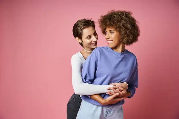 stock image happy woman embracing her african american girlfriend on pink background, lgbtq couple love