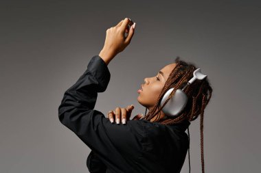 african american woman with dreadlocks listening music in headphones and looking away on grey clipart