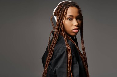 Gri arka planda kulaklıkla müzik dinleyen hoş Afrikalı Amerikalı kadın.