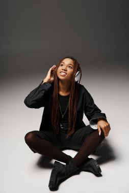 Carefree african american girl with dreadlocks enjoying the beat in wireless headphones on grey clipart