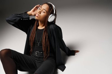 20 'li yaşlarda Afro-Amerikan bir kadın. Gözleri kapalı, kulaklıkla müzik dinliyor ve gri renkte oturuyor.