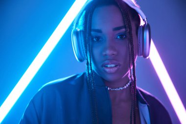 portrait of african american girl in dreadlocks and headphones in studio with blue fluorescent light clipart