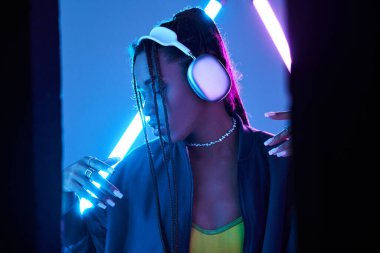 pretty african american woman in headphones enjoying music in studio with blue fluorescent light clipart