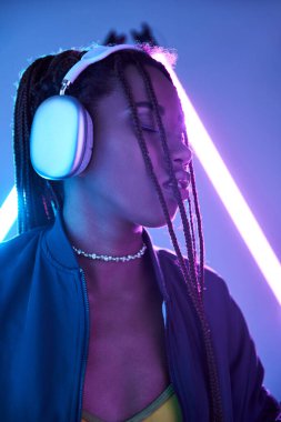 Güzel Afro-Amerikalı kulaklıklı kadın stüdyoda floresan ışığıyla müzik dinliyor.