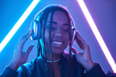 Neşeli Afro-Amerikalı kulaklıklı kadın stüdyoda floresan ışığıyla müzik dinliyor.