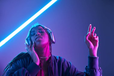 Kendinden geçmiş Afro-Amerikalı kulaklıklı kadın stüdyoda floresan ışığıyla müzik dinliyor.
