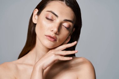 A young, caucasian woman with brunette hair and clean skin posing nude with her eyes gently closed in a studio setting. clipart