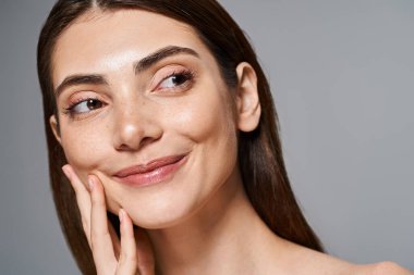 A young Caucasian woman smiling warmly with her hand elegantly resting on her face, showcasing joy and comfort. clipart