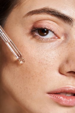 Temiz ciltli beyaz bir kadının kozmetik pipetle serum uyguladığı yakın plan bir fotoğrafı.