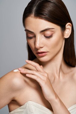 A young woman with brunette hair poses gracefully in a strapless dress, her hands delicately touching cream on shoulder clipart