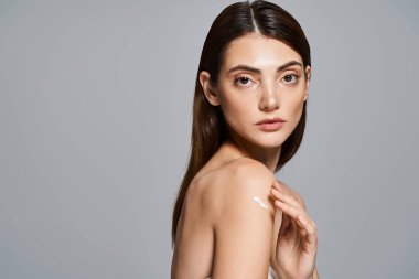 Uzun esmer saçlı beyaz bir kadın stüdyo ortamında zarif pozlar veriyor, omuzlarında kremayla.