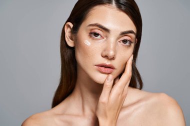 A young Caucasian woman with brunette hair applies a white cream on her face in a studio setting. clipart