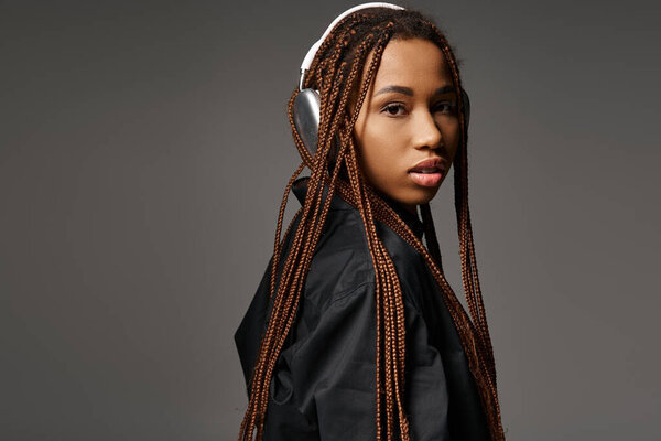 pretty african american woman with dreadlocks listening music in headphones on grey background