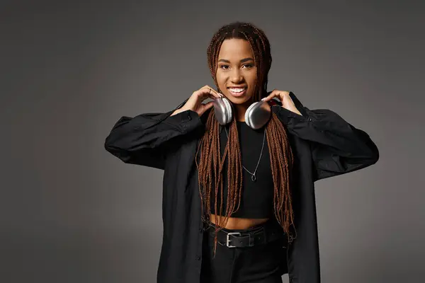 stock image smiling african american woman with dreadlocks standing in headphones and looking at camera on gray