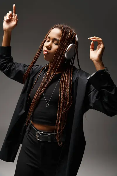 ecstatic dance of young african american woman with dreadlocks and wireless headphones on grey