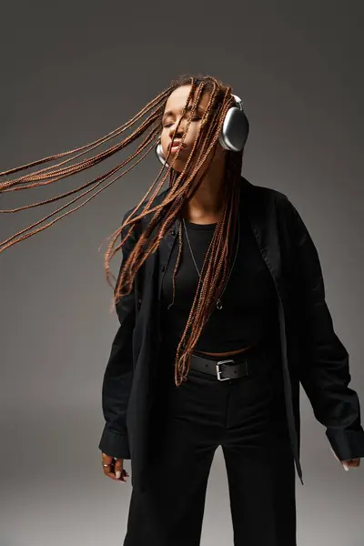 ecstatic dance of carefree african american woman with dreadlocks and wireless headphones on grey