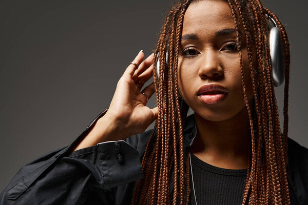 портрет беззаботной африканской женщины в возрасте 20 лет с дредами и беспроводными наушниками на сером