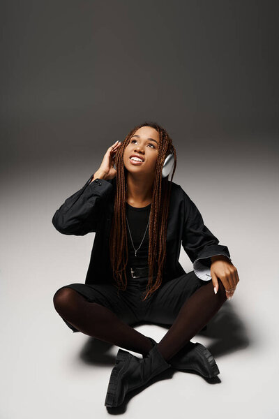 Carefree african american girl with dreadlocks enjoying the beat in wireless headphones on grey