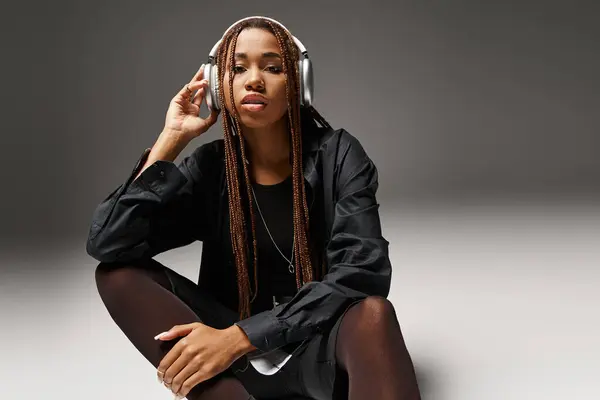 stock image young african american woman in 20s with dreadlocks enjoying music in stylish headphones on grey