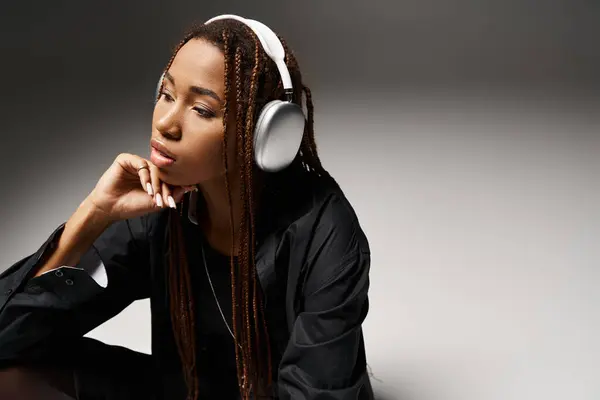 stock image pensive african american woman in 20s with dreadlocks listening music in headphones in grey studio