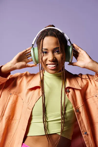 stock image happy african american girl in 20s wearing headphones and vibrant casual attire on purple background